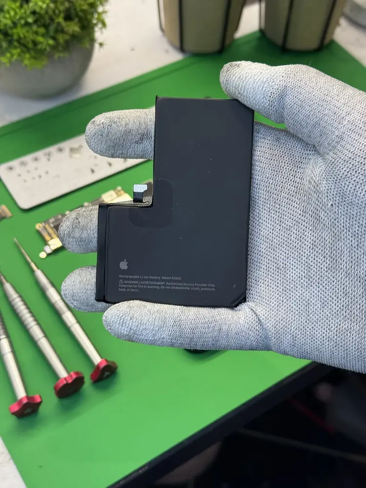 Bateria iPhone w dłoni, wkrętaki na macie