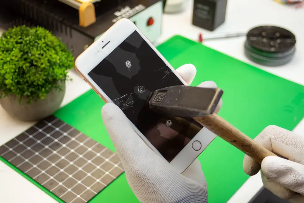 iPhone z pękniętym ekranem i młotek na stanowisku