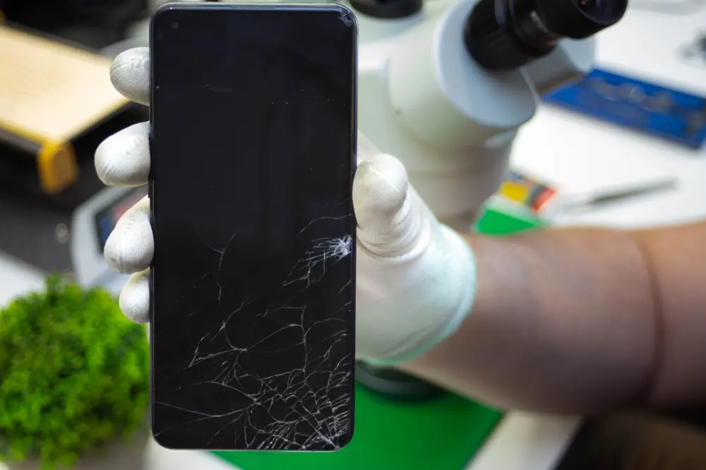 Telefon z pękniętym ekranem w dłoni, w tle mikroskop
