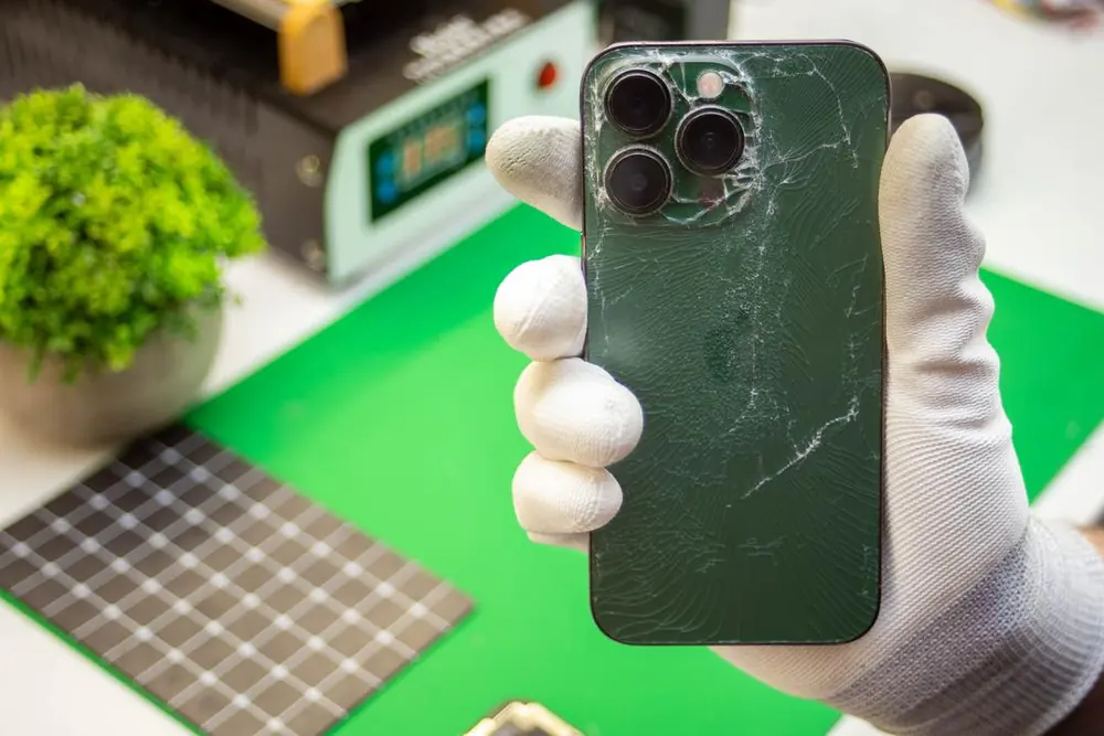 Zielony iPhone Pro z pękniętą tylną szybą w dłoni